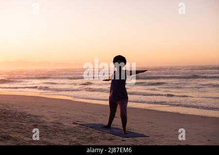 Silhouette afroamerikanische reife Frau praktizierende Kriegerin 2 Pose am Strand gegen klaren Himmel Stockfoto