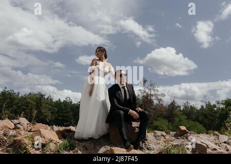 Romantisches Hochzeitspaar, das bei Sonnenuntergang auf den Bergen posiert und eine fantastische Aussicht bietet. Wunderschöne Brautpaar an ihrem Hochzeitstag. Hochwertige Fotos Stockfoto