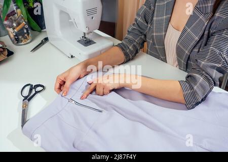 Porträt einer Näherin in einer karierten Jacke, die in ihrem Nähstudio arbeitet, und zeigt die Innenseite des Kleidungsfutters Stockfoto