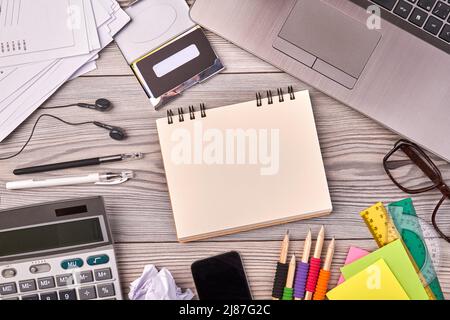 Von oben gesehen lag der flache, leere Notizblock und Bürosachen auf dem Schreibtisch. Taschenrechner mit Brille und Laptop. Stockfoto