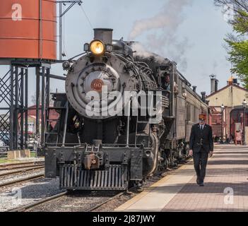 Strasburg Pennsylvania-22. April 2022: Zugbegleiter läuft neben dem Dampfzug, als er den Bahnhof in Strasburg, Lancaster County, Pennsylvania, erreicht Stockfoto