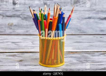 Gelber Halter voller Stifte und Stifte. Weißer Schreibtisch-Hintergrund. Stockfoto