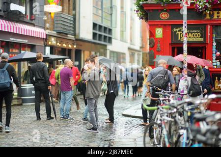 DUBLIN, IRLAND - MAI 2018: Geschäftiges Alltagsleben von Touristen und Stadtbewohnern in Dublin, Irland. Menschen, die an einem regnerischen Tag am berühmten Temple Bar Pub vorbei laufen. Stockfoto