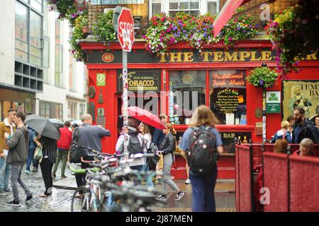 DUBLIN, IRLAND - MAI 2018: Geschäftiges Alltagsleben von Touristen und Stadtbewohnern in Dublin, Irland. Menschen, die an einem regnerischen Tag am berühmten Temple Bar Pub vorbei laufen. Stockfoto