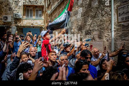 Jerusalem, Israel. 13.. Mai 2022. Ein palästinensischer Junge schwingt während der Trauerprozession eine palästinensische Fahne. Abu Aklei wurde am Mittwochmorgen im besetzten Westjordanland getötet, als sie einen israelischen Angriff auf die Stadt Jenin verdeckte. Zeugen sagten, dass sie von einem israelischen Soldaten getötet wurde. Die israelische Armee sagte am Freitag, dass Frau Abu Aklei, obwohl es möglich war, versehentlich durch einen israelischen Brand getötet wurde; ihre ersten Ermittlungen lassen vermuten, dass sie auch von einem palästinensischen Schützen getroffen worden sein könnte. (Foto von Eyal Warshavsky/SOPA Images/Sipa USA) Quelle: SIPA USA/Alamy Live News Stockfoto