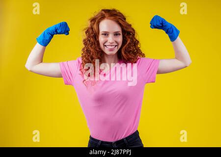 Rothaarige lockige Ingwer Frau zeigt Training Hände Muskeln in Studio gelb Hintergrund Wand Stockfoto