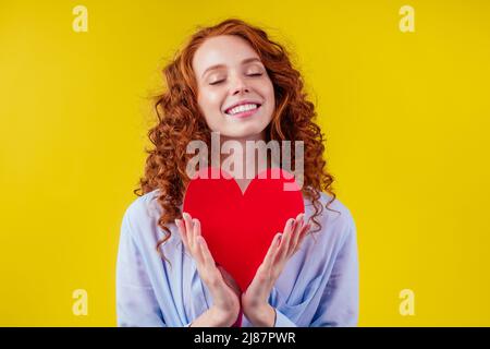 Schwanger Rotschopf Ingwer lockig Frau hält Papier Herz in Studio gelbe Wände.Valentinstag Stockfoto