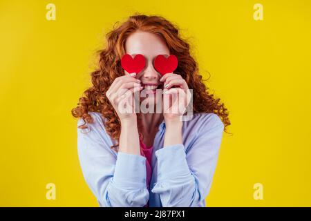 Schwanger Rotschopf Ingwer lockig Frau hält Papier Herz in Studio gelbe Wände.Valentinstag Stockfoto