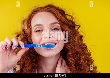 Verschmattete rothaarige Ingwer-Frau putzt Zähne mit Zahnpasta Öko-Paste auf gelbem Studiohintergrund Stockfoto