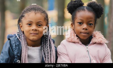 Portrait Jugendliche niedliche Kinder Nahaufnahme zwei Schwestern verbringen Zeit im Stadtpark kleine Freunde schauen auf die Kamera glücklich lächelnde kleine Mädchen sitzen auf Stockfoto