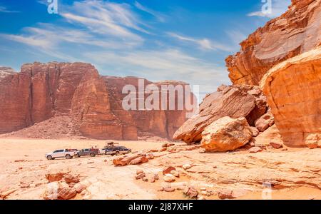 Rote Steine und Felsen der Wadi Rum Wüste mit Autos im Hintergrund, Jordanien Stockfoto