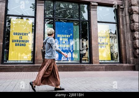 Kiew, Ukraine. 13.. Mai 2022. Eine Frau kommt an großen Schildern in den Schaufenstern vorbei, auf denen steht: „Die Marke der Ukraine ist tader“ und „die in der Ukraine hergestellte tader“. Kredit: SOPA Images Limited/Alamy Live Nachrichten Stockfoto