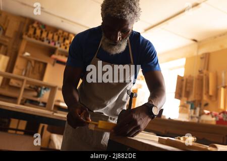 afroamerikanischer reifer Zimmermann in Schürze, der in der Werkstatt arbeitet Stockfoto