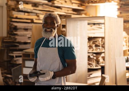 Porträt eines lächelnden afroamerikanischen, reifen Zimmermanns in der Schürze in der Werkstatt Stockfoto