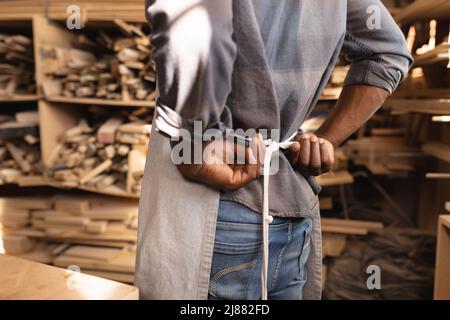 Mittelteil eines afroamerikanischen, reifen Zimmermanns, der Schürze trägt, während er in der Werkstatt arbeitet Stockfoto