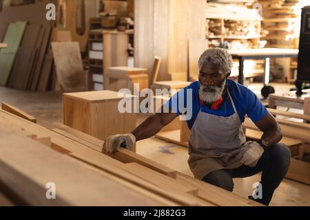 afroamerikanischer reifer Zimmermann, der Planken in der Werkstatt untersucht Stockfoto