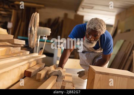 afroamerikanischer reifer Zimmermann, der Planken während der Arbeit in der Werkstatt untersucht Stockfoto