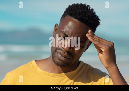 Nahaufnahme eines jungen afroamerikanischen Mannes mit geschlossenen Augen, der im Sommer den Kopf am Strand gegen den Himmel berührt Stockfoto