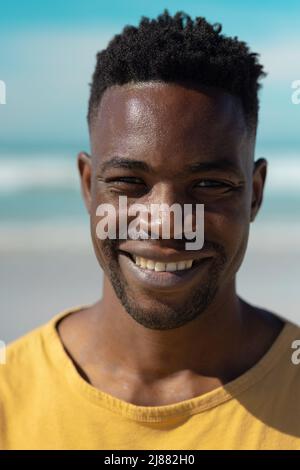 Nahaufnahme des lächelnden, hübschen afroamerikanischen jungen Mannes am Strand gegen den Himmel an einem sonnigen Tag Stockfoto