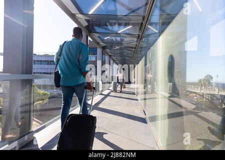 Junger afroamerikanischer Geschäftsmann mit Gepäck, der am Flughafen hinter einer Geschäftsfrau herläuft Stockfoto