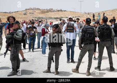 Masafer Yatta, Palästina. 13.. Mai 2022. Polizeibeamte stehen vor Demonstranten und halten Plakate zum Gedenken an den langjährigen Journalisten Shireen Abu Aklei, der von den israelischen Streitkräften getötet wurde, als er einen israelischen Überfall in der Stadt Jenin verdeckte. Ein Solidaritätsprotest israelischer Friedensaktivisten und Bewohner von Masafer Yatta, die einer sofortigen Abschiebung drohen. Ein kürzlich erteiltes Urteil des israelischen Obersten Gerichts über die seit langem andauende Vertreibung von acht Gemeinden unter diesen ist Masafer Yatta in Palästina. Kredit: SOPA Images Limited/Alamy Live Nachrichten Stockfoto
