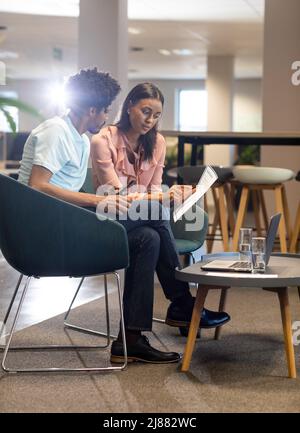 Selbstbewusste junge Birazialkollegen diskutieren über Dokumente, während sie am Arbeitsplatz zusammen sitzen Stockfoto