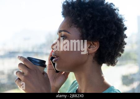 Junge afroamerikanische Geschäftsfrau hält Kaffeetasse im Gespräch auf dem Smartphone Stockfoto