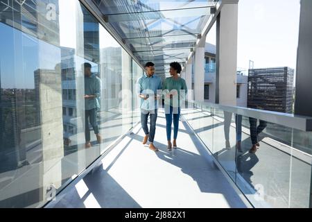 Die ganze Länge der lächelnden afroamerikanischen Kollegen diskutieren, während sie am Arbeitsplatz im Flur spazieren Stockfoto