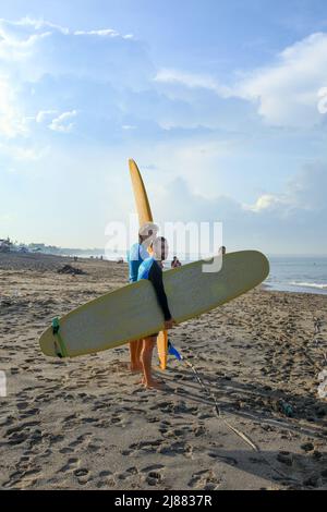 Zwei kaukasische Surfer stehen am Batu Bolong Beach in Canggu, Bali, Indonesien, mit ihren langen Boards oder malibu Surfbrettern. Stockfoto