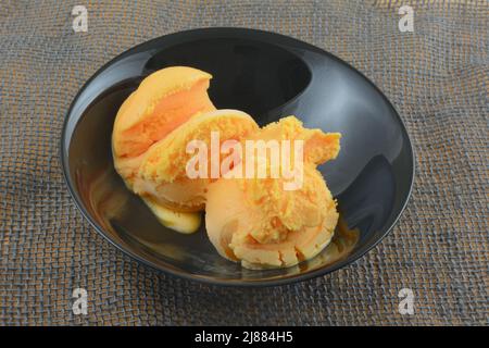 Zwei Kugeln orangefarbenem Sherbet mit Schokoladensirup in schwarzer Schale auf grauem Elop Stockfoto