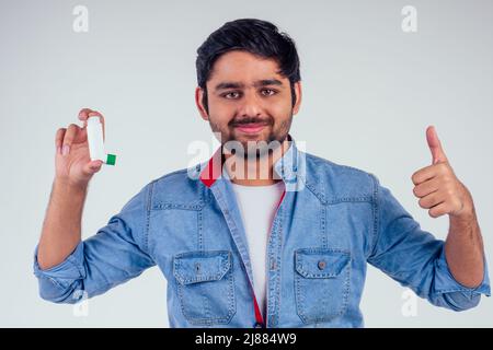 Junger inder in einer Jeansjacke mit Asthma-Inhalator auf weißem Hintergrund im Studio Stockfoto