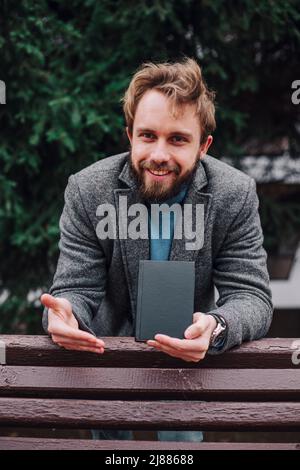 Portrait schöner bärtiger Mann mit Brille blaues Hemd.Mann in der Nähe der Universitätsbibliothek, Buch lesen und entspannen. Unscharfer Hintergrund.Horizontal, Film e Stockfoto