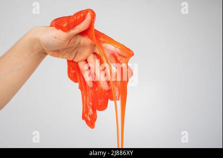 Roter Schleim, der aus der Hand einer Frau auf einem weißen Hintergrund herabfließt. Stockfoto