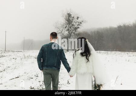 Braut und Bräutigam halten die Hände, die im Winter nach der Zeremonie den Weg hinunter gehen Stockfoto