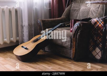 Ein Stapel alter Vinyl-Schallplatten und eine akustische Holzgitarre mit Verstärker sind auf einem braunen Hintergrund für ein Musik- oder Bandkonzept isoliert. Stockfoto