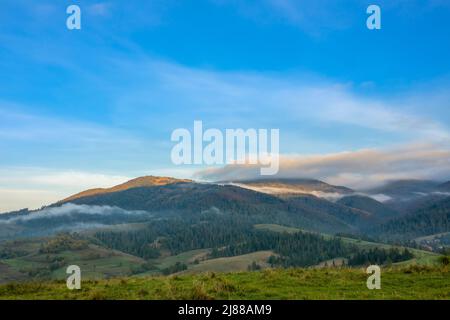 Sommer ukrainischen Karpaten und sonnigen Morgen. Leichter Nebel zwischen bewaldeten Bergen. Die ersten Sonnenstrahlen erleuchten die Berggipfel Stockfoto