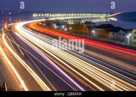 Vorstädtische ukrainische Autobahn am Abend. Spuren von Scheinwerfern und Schlussleuchten von starkem Verkehr und Ampeln auf der Brücke Stockfoto