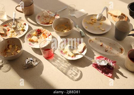 Nach dem Essen schmutzige Teller mit Löffeln und Gabeln auf dem Tisch leeren. Konzept für Bankettende. Ungewaschene Gerichte, die zur Reinigung bereit sind Stockfoto