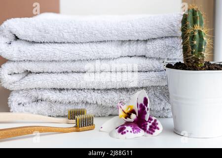 Bambuszahnbürsten auf einem Hintergrund aus weißen Baumwollhandtüchern mit einer Orchideenblume und einem grünen Kaktus. Stockfoto