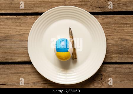 Ein weißes Hühnerei mit einer bemalten Flagge der Ukraine auf einem Teller und einer Kugel auf dem Tisch zu Hause, Kultur und Schutz Ihres Hauses 2022 Stockfoto