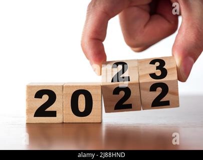 Neujahrskonzept von 2022 bis 2023. Die Hand des Mannes wechselt Holzwürfel auf dem weißen Tisch. Wandel, Erfolg und neue Geschäftspläne Stockfoto