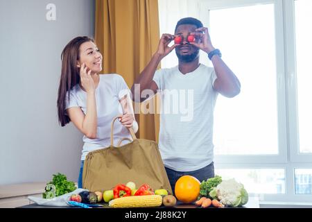 Multinationales Paar entlädt eine Tasche aus Produkten, die Textil- oder Polyestertasche wählen.african american Mann und asiatische Frau kommen nach dem Laden nach Hause Stockfoto