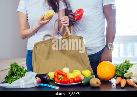 Multinationales Paar entlädt eine Tasche aus Produkten, die Textil- oder Polyestertasche wählen.african american Mann und asiatische Frau kommen nach dem Laden nach Hause Stockfoto