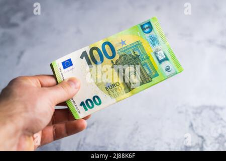 Hand halten und geben hundert 100-Euro-Banknoten. Geld in Menschenhand auf grauem Hintergrund Stockfoto