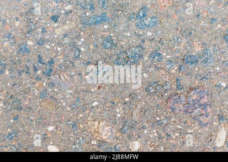 Textur von altem, abgedonnenen Asphalt. Freiliegende bläuliche Kieselsteine, die aus der Dicke des Asphalts spähen. Stockfoto