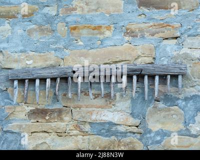 Alte Holzrechen, die an einer Steinmauer eines Landhauses hängen, Beispiel für traditionelle landwirtschaftliche Werkzeuge Stockfoto