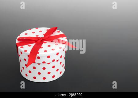 Geschenkschachtel mit Punktmuster und roter Schleife auf grauem Hintergrund. Luxus Geschenk geben Konzept für Geburtstag, Jubiläum, Weihnachten, Muttertag. Stockfoto