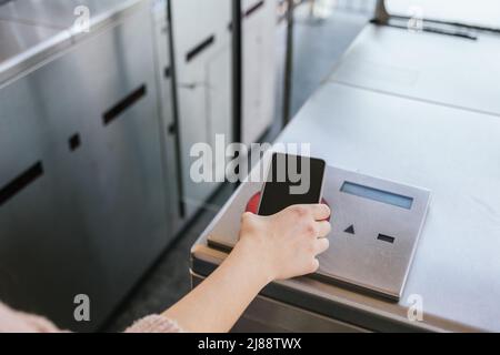 Mädchen, die ihr Zugticket mit ihrem Mobiltelefon auf dem Bahnhof durch den Automaten führt. NFC- und kontaktloses Technologiekonzept Stockfoto