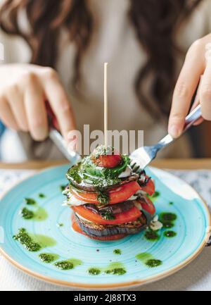 Blick auf eine Frau, die auf einem Teller Auberginen und Tomatenballen isst. Leckeres und gesundes Essen im Restaurant Stockfoto