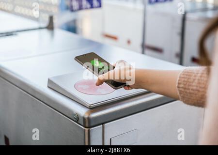 Die Hand der Frau tickt ihr Transportticket in der Maschine mit ihrem Mobiltelefon am Bahnhof. NFC- und kontaktloses Technologiekonzept Stockfoto